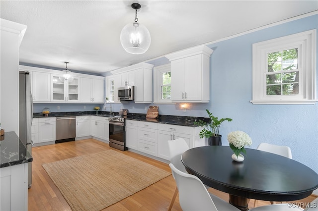 kitchen with pendant lighting, white cabinetry, stainless steel appliances, and light hardwood / wood-style flooring