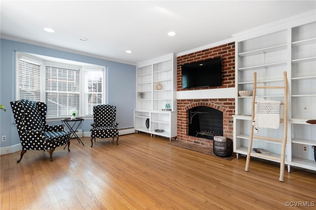 sitting room featuring built in shelves, hardwood / wood-style flooring, ornamental molding, and a brick fireplace