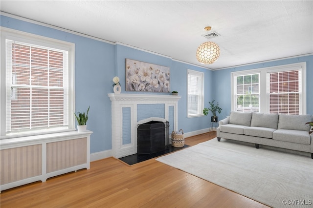 living room featuring hardwood / wood-style flooring, a brick fireplace, radiator, and ornamental molding