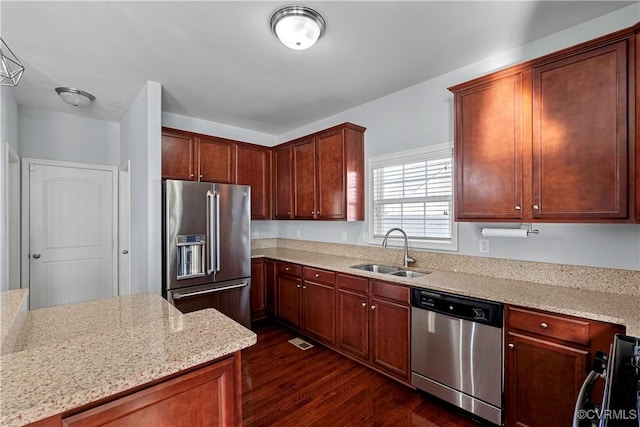 kitchen with appliances with stainless steel finishes, dark wood-type flooring, light stone counters, and sink