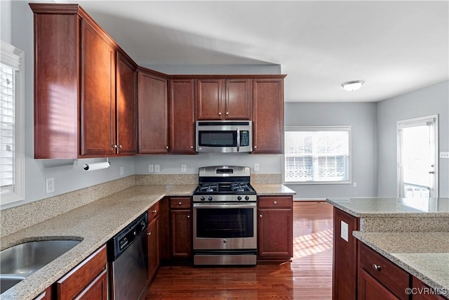 kitchen featuring appliances with stainless steel finishes, dark hardwood / wood-style flooring, light stone counters, and sink