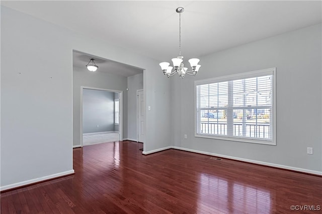 empty room with dark hardwood / wood-style flooring and an inviting chandelier