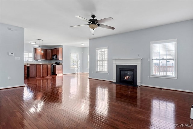 unfurnished living room with ceiling fan, dark wood-type flooring, and plenty of natural light