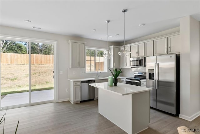 kitchen with backsplash, hanging light fixtures, light wood-type flooring, appliances with stainless steel finishes, and a kitchen island