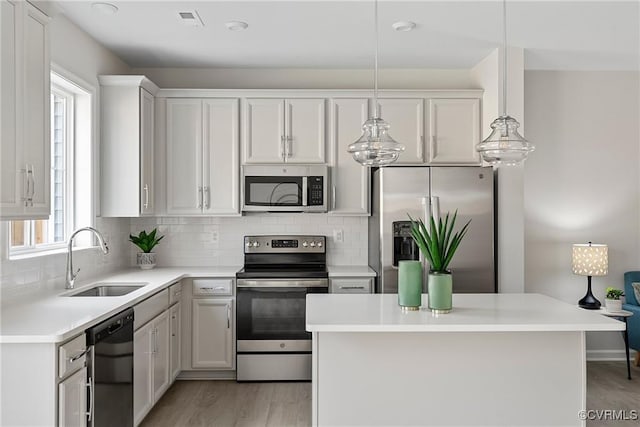 kitchen with white cabinetry, sink, stainless steel appliances, light hardwood / wood-style floors, and pendant lighting