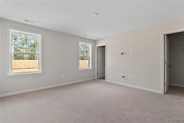 unfurnished bedroom featuring multiple windows, a walk in closet, and light carpet