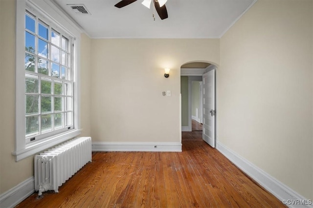 spare room with arched walkways, wood finished floors, visible vents, baseboards, and radiator