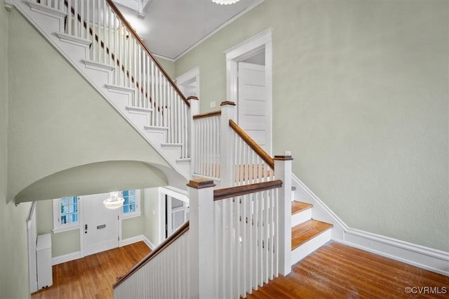 stairway with ornamental molding, arched walkways, baseboards, and wood finished floors