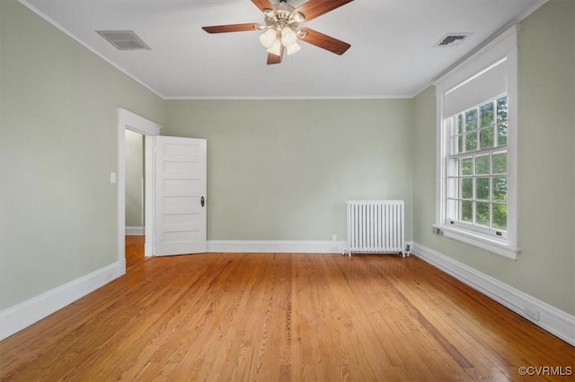 spare room with baseboards, light wood-style floors, ornamental molding, and radiator