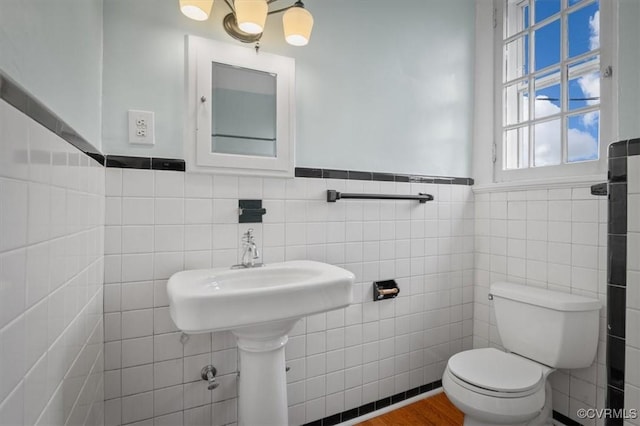 bathroom featuring a wainscoted wall, tile walls, toilet, and wood finished floors