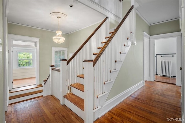 staircase with ornamental molding, radiator, a chandelier, and wood finished floors