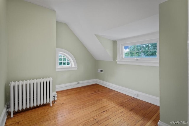 additional living space with vaulted ceiling, baseboards, hardwood / wood-style flooring, and radiator