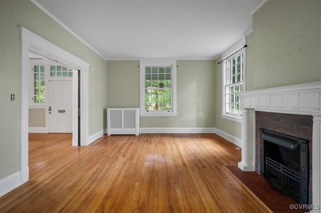 unfurnished living room with radiator heating unit, a fireplace with flush hearth, hardwood / wood-style flooring, and baseboards