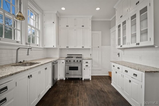 kitchen featuring stainless steel appliances, a sink, white cabinets, light stone countertops, and glass insert cabinets