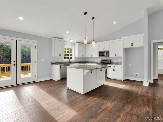 kitchen with appliances with stainless steel finishes, dark stone counters, vaulted ceiling, white cabinets, and a center island