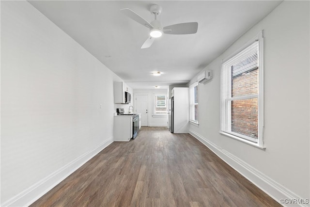 unfurnished living room with a wall unit AC, ceiling fan, and dark wood-type flooring