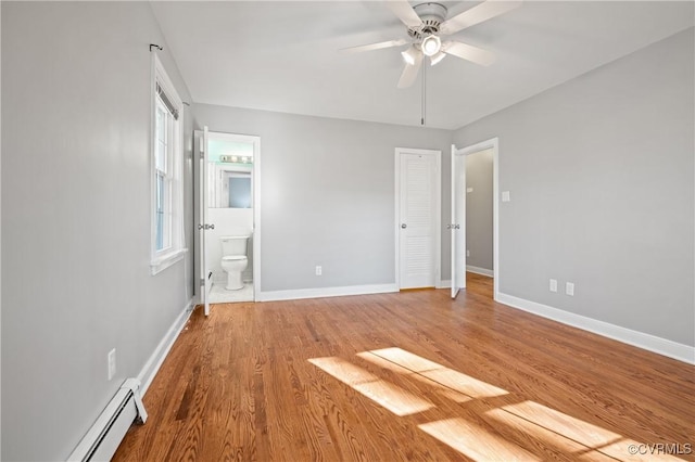 unfurnished bedroom with baseboard heating, connected bathroom, multiple windows, hardwood / wood-style flooring, and ceiling fan