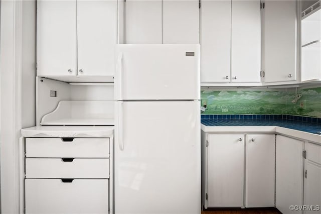 kitchen with white refrigerator, white cabinetry, and tasteful backsplash