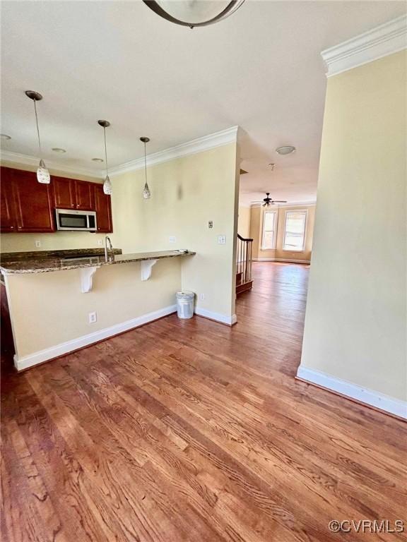 kitchen featuring dark hardwood / wood-style floors, decorative light fixtures, a breakfast bar area, ornamental molding, and kitchen peninsula