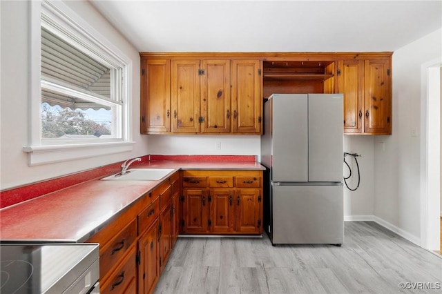 kitchen featuring stainless steel fridge, light wood-type flooring, range, and sink