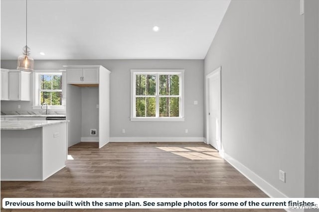 kitchen with light stone countertops, white cabinetry, baseboards, and wood finished floors