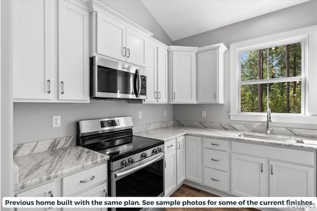 kitchen with lofted ceiling, light stone counters, stainless steel appliances, a sink, and white cabinets