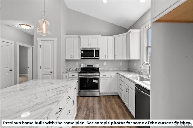 kitchen featuring appliances with stainless steel finishes, light stone countertops, vaulted ceiling, white cabinetry, and a sink