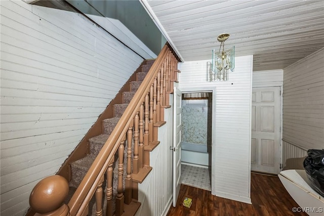 staircase with wood-type flooring, wood ceiling, wood walls, and a chandelier