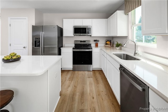 kitchen featuring white cabinets, appliances with stainless steel finishes, sink, light wood-type flooring, and a breakfast bar area