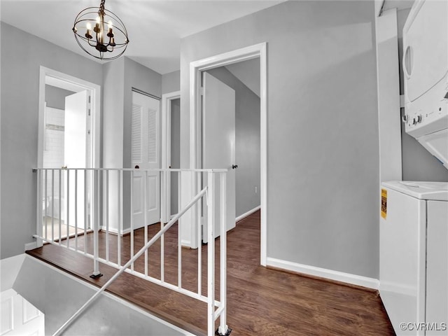 staircase with stacked washer and dryer, wood-type flooring, and a notable chandelier