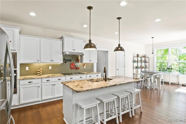 kitchen featuring sink, white cabinetry, decorative light fixtures, an island with sink, and light stone countertops