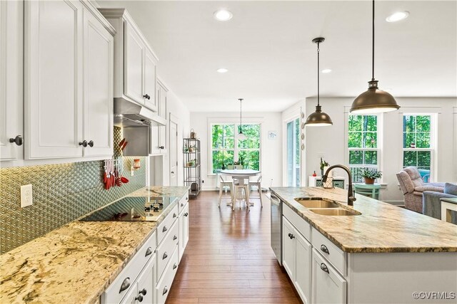 kitchen with sink, white cabinetry, hanging light fixtures, a center island with sink, and light stone countertops