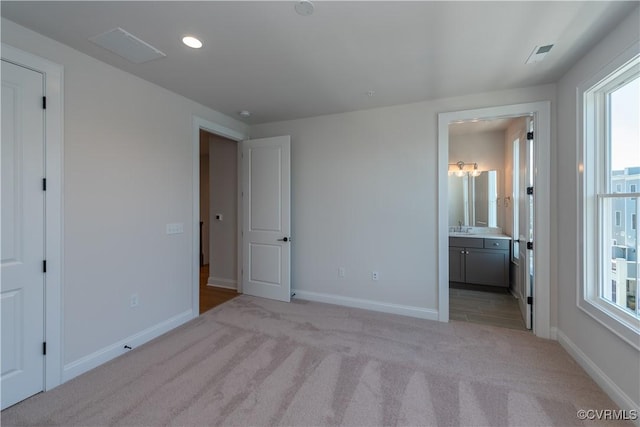 unfurnished bedroom with ensuite bathroom, sink, and light colored carpet