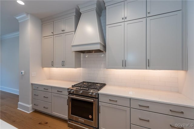 kitchen featuring backsplash, premium range hood, gray cabinetry, light hardwood / wood-style floors, and stainless steel range with gas stovetop