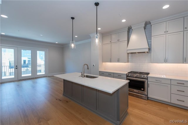 kitchen with sink, hanging light fixtures, a kitchen island with sink, high end stainless steel range, and custom range hood