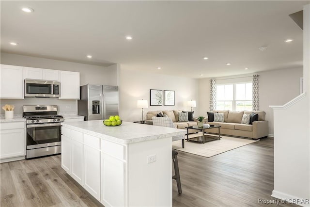 kitchen featuring white cabinets, appliances with stainless steel finishes, a kitchen island, a breakfast bar, and light hardwood / wood-style flooring