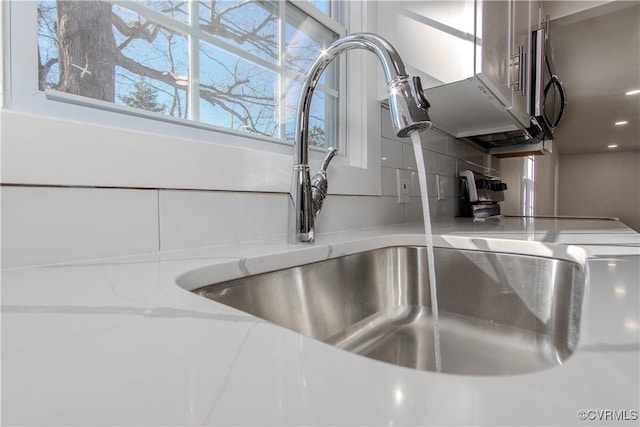 interior details featuring white cabinets, light stone counters, and sink