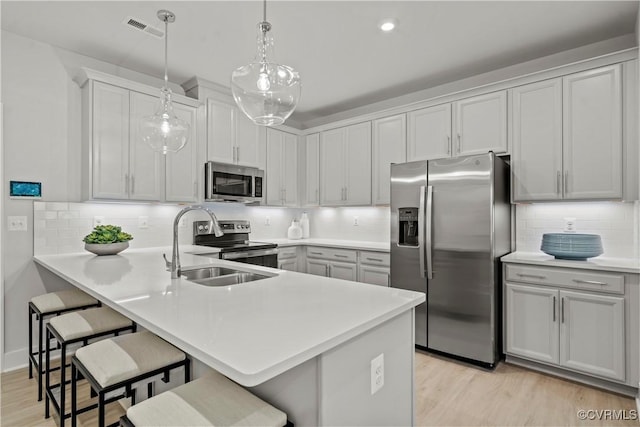 kitchen with hanging light fixtures, sink, appliances with stainless steel finishes, kitchen peninsula, and a breakfast bar area