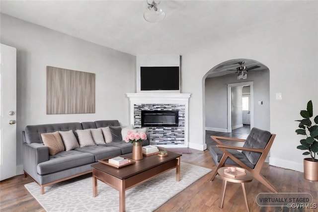 living room with a tile fireplace, ceiling fan, and dark wood-type flooring