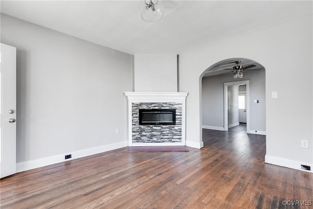 unfurnished living room with a tile fireplace, ceiling fan, and dark wood-type flooring