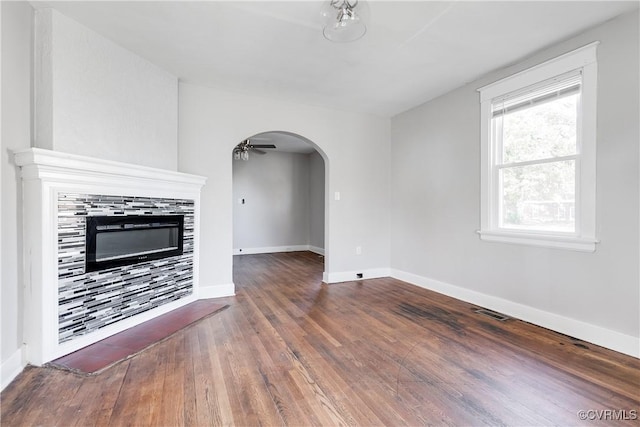 unfurnished living room featuring a tile fireplace, ceiling fan, and dark wood-type flooring