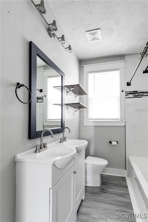 full bathroom with vanity, a textured ceiling, toilet, and a healthy amount of sunlight