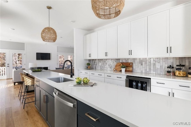 kitchen with stainless steel dishwasher, pendant lighting, beverage cooler, white cabinets, and sink