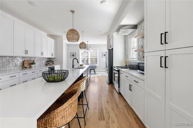 kitchen with hanging light fixtures, stainless steel appliances, an island with sink, white cabinets, and sink