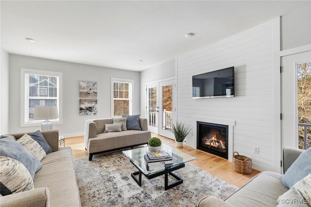 living room with a fireplace, light wood-type flooring, french doors, and a healthy amount of sunlight