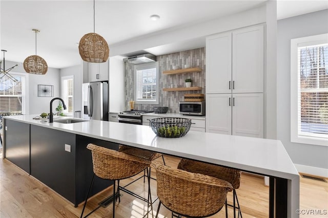 kitchen with sink, white cabinets, pendant lighting, a kitchen island with sink, and appliances with stainless steel finishes