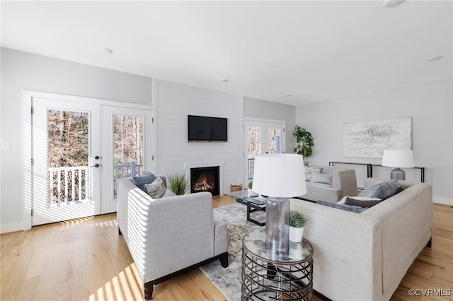 living room with a large fireplace, light wood-type flooring, french doors, and plenty of natural light