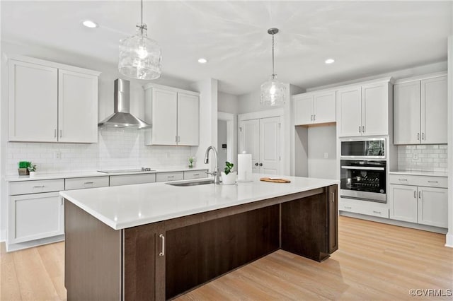 kitchen with wall chimney range hood, sink, appliances with stainless steel finishes, decorative light fixtures, and white cabinetry