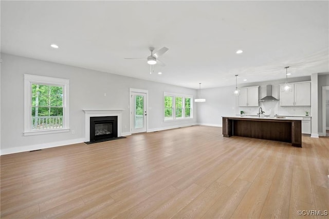 unfurnished living room featuring ceiling fan, light wood-type flooring, and sink