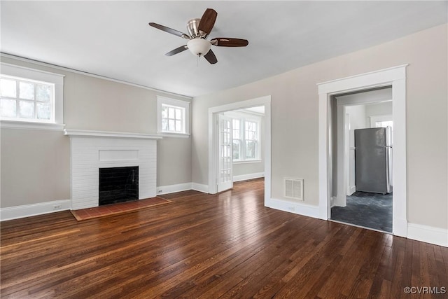 unfurnished living room featuring ceiling fan, a brick fireplace, and dark hardwood / wood-style flooring